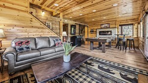 A cozy log cabin interior with a sofa, coffee table, fireplace, and pool table.
