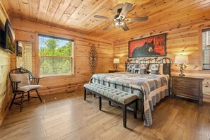 Een gezellig slaapkamer in een houten chalet, met een bed met een geborduurde deken, een bankje, een stoel en een schilderij van een beer.