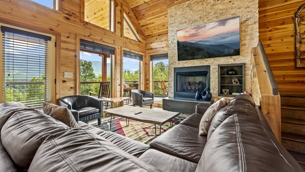 A cozy log cabin interior with a fireplace, leather sofa, and a dining area.