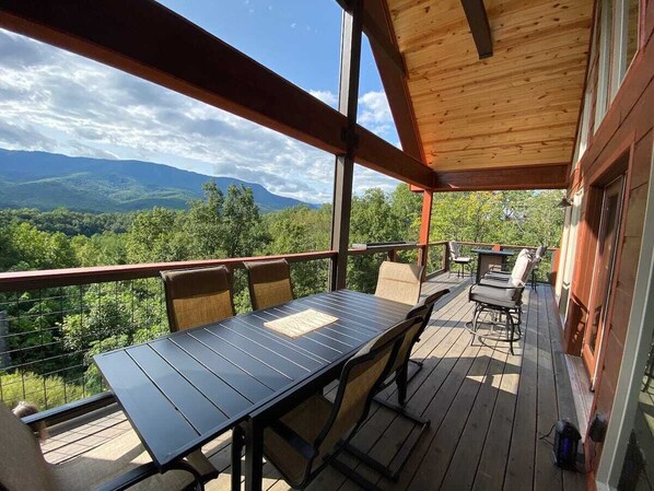 Een overdekt terras buiten met een tafel en stoelen, met uitzicht op een bergachtig landschap.