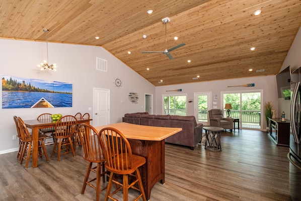 A spacious living area with a wooden ceiling, a dining table with chairs, a sofa, and a television. - RIVER FRONT HOME AMAZING VEIWS AND HOT TUB (Shenandoah)