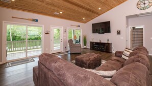 A spacious living room with a wooden ceiling, a large flat-screen TV, and a cozy brown sectional sofa. - RIVER FRONT HOME AMAZING VEIWS AND HOT TUB (Shenandoah)