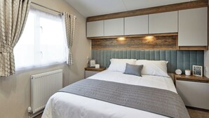 Un dormitorio con cama, mesita de noche, ventana con cortinas, radiador y cabecera de madera.