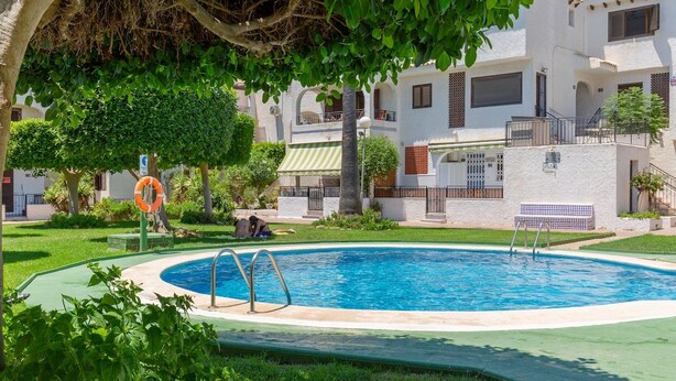 A swimming pool surrounded by greenery and a white building with balconies. - Flamingo Coast by Fidalsa (La Zenia)