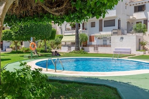 Une piscine entourée de verdure et un bâtiment blanc doté de balcons.