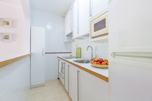 Une cuisine de taille réduite avec des meubles blancs, un plan de travail en bois, un évier et un four à micro-ondes.