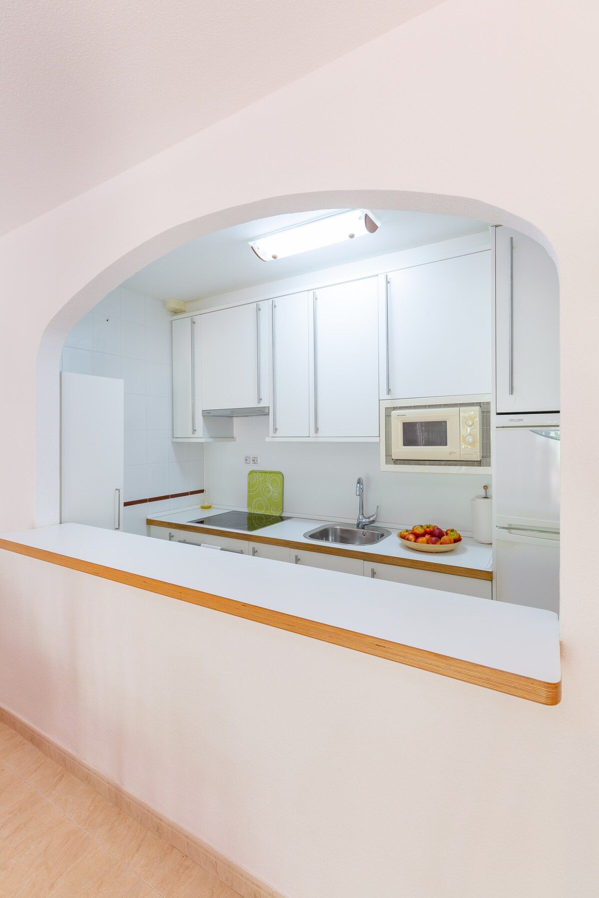 A kitchen with white cabinets, a microwave, a sink, and a fruit bowl on the counter.