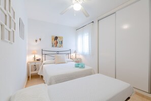 Slaapkamer met twee bedden, een plafondventilator, een schilderij aan de muur en een raam met gordijnen.
