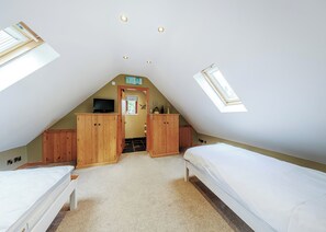 Une chambre avec deux lits, des armoires en bois, une télévision et un puits de lumière.