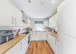 A modern kitchen with white cabinets, a wooden countertop, a built-in oven, and a window with a view of greenery. - Lower Lake Boathouse (Anglesey)