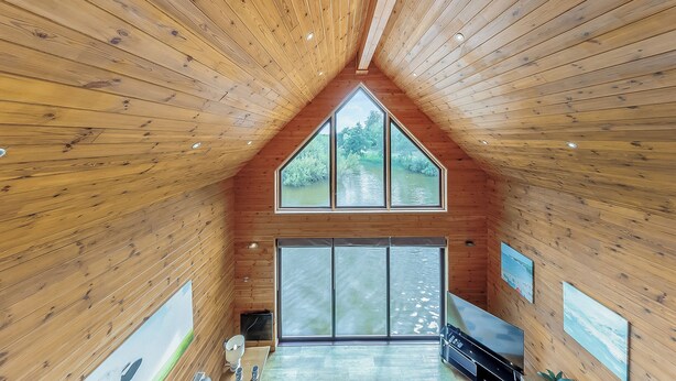 A wooden interior with a sloped ceiling, large windows, and a view of greenery outside. - Lower Lake Boathouse (Anglesey)