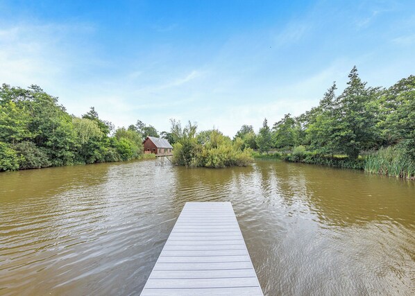 A wooden dock extending into a river with a house on the opposite bank. - Lower Lake Boathouse (Anglesey)