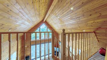 Ein Holzinnenraum mit schrägverdeckter Decke, einem Balkon mit Geländer und Blick ins Freie.