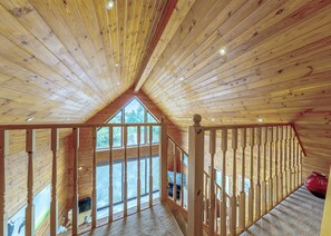 Un intérieur en bois avec un plafond incliné, un balcon doté d’une balustrade et une vue sur l’extérieur.