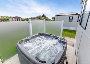 A hot tub with a wooden deck, surrounded by a fence, and adjacent to a building with a tiled roof. - Luxurious holiday home. (Looe)