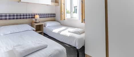 Habitación de hotel con dos camas, una ventana con cortinas, una mesita de noche con lámpara y un cabecero de madera.