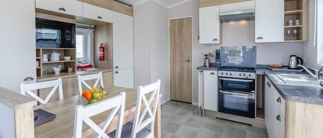 Una cocina moderna con armarios blancos, una mesa de comedor con sillas y un horno empotrado.