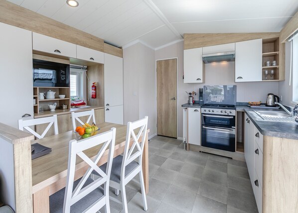 A modern kitchen with white cabinetry, a dining table with chairs, and a built-in oven.