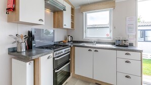 A modern kitchen with a stove, oven, sink, and a window with a view of the outside. - Luxurious holiday home. (Looe)