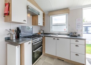 A modern kitchen with a stove, oven, sink, and a window with a view of the outside.