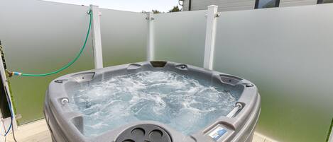 Un jacuzzi con panel de control, rodeado por una terraza de madera y una valla verde.