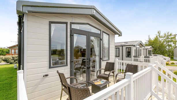 A mobile home with a deck, wicker furniture, and a white railing. - Luxurious holiday home. (Looe)