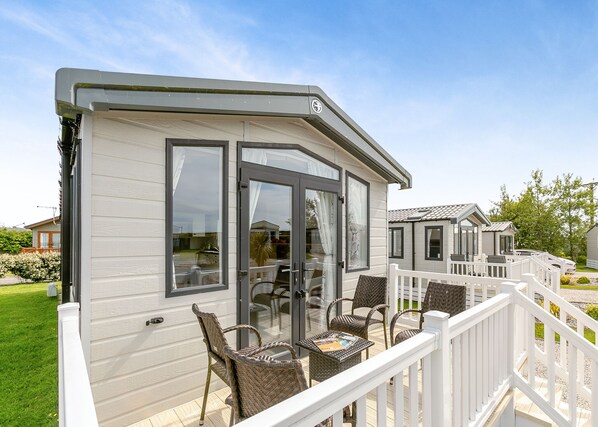 A mobile home with a deck, wicker furniture, and a white railing.