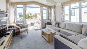 A cozy living room with a sofa, chairs, a coffee table, and a TV. - Luxurious holiday home. (Looe)