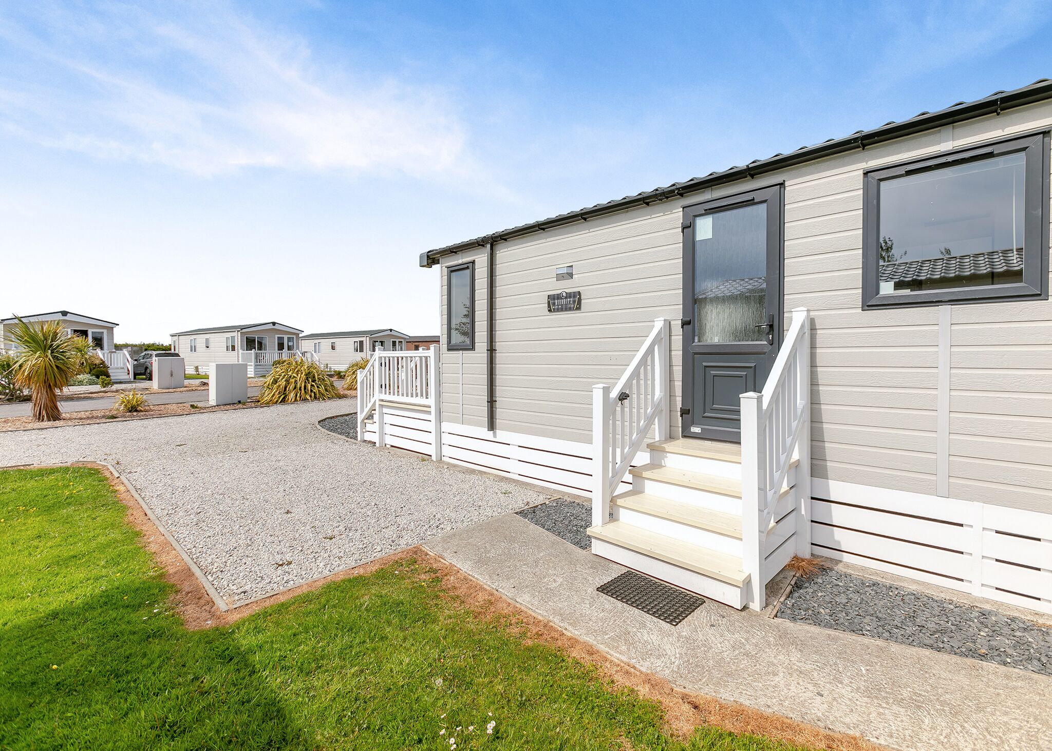 A mobile home with a front porch, steps, and a gravel driveway.