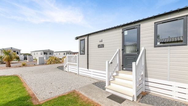 A mobile home with a front porch, steps, and a gravel driveway.