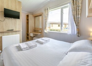 A hotel room with a bed, a TV mounted on the wall, a window with curtains, and a wooden wardrobe.