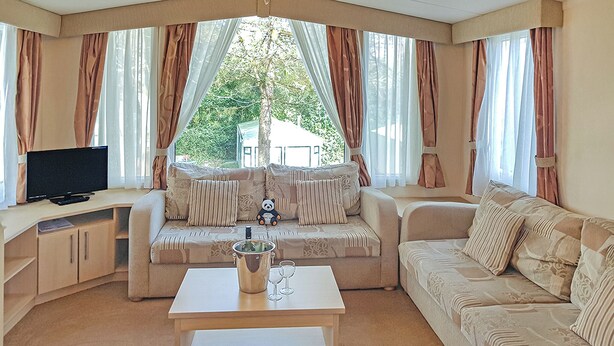 A living room with a sofa, a television, a coffee table with a bottle and glasses, and curtains.