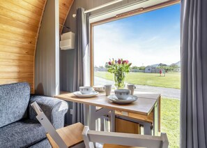 A cozy interior with a wooden ceiling, a table with a vase of flowers, and a view of a grassy field.