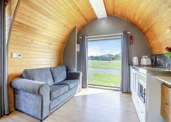 A cozy cabin interior with a sofa, kitchenette, and a large window offering a view of the outdoors. - 1 bedroom accommodation in Great Busby (Great Busby)