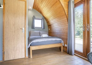 A bedroom with a wooden ceiling, a bed, a window with curtains, and a door.