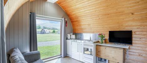 A compact kitchen with a built-in oven, a flat-screen TV, and a window overlooking a grassy area.
