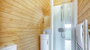 Un bagno con rivestimento in legno, cabina doccia in vetro, lavandino e water.