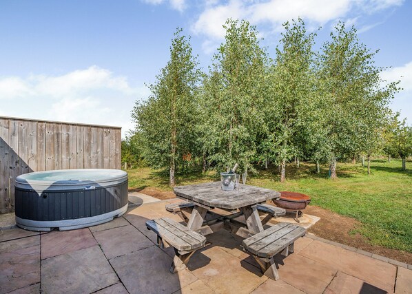 A hot tub, picnic table, and chairs in a backyard with a wooden fence and trees.