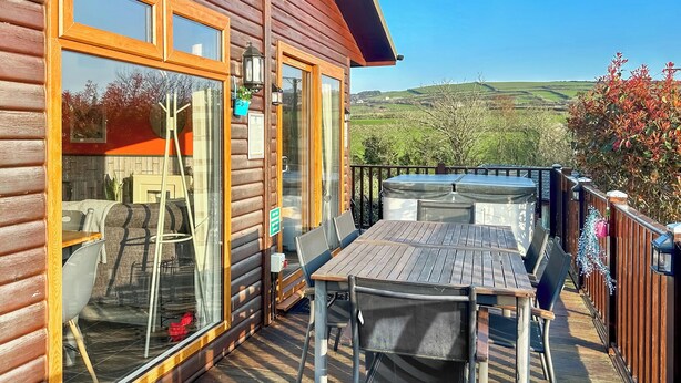 A wooden cabin with a deck, a table, and chairs. - Country Lodge Six Spa (Tintagel)