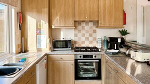 A compact kitchen with wooden cabinets, a microwave, a stove, an oven, a sink, and a toaster. - Country Lodge Six Spa (Tintagel)