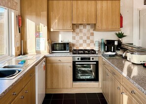 A compact kitchen with wooden cabinets, a microwave, a stove, an oven, a sink, and a toaster.