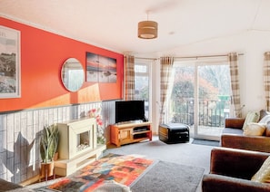 A living room with a fireplace, TV, sofa, and large windows. - Country Lodge Six Spa (Tintagel)