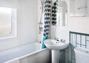 A bathroom with a bathtub, a sink, a toilet, a window, and a shower curtain.