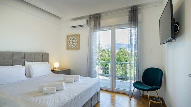 Quarto de hotel com uma cama grande, televisão na parede, uma cadeira e varanda com vista.
