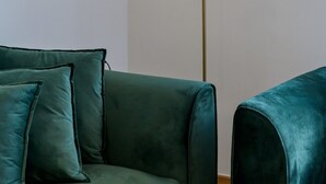 Um quarto com um sofá verde-turquesa, um candeeiro de chão com luz redonda e um espelho na parede.