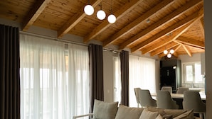 A modern living room with a wooden ceiling, a grey sofa, and a dining area with chairs and a table. - Angel Saranda Palace (Sarandë)