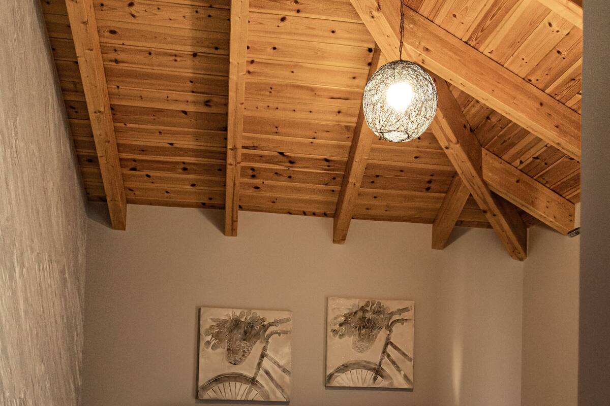 A bedroom with a wooden ceiling, a bed with white linens, two wall-mounted artworks, and a nightstand.