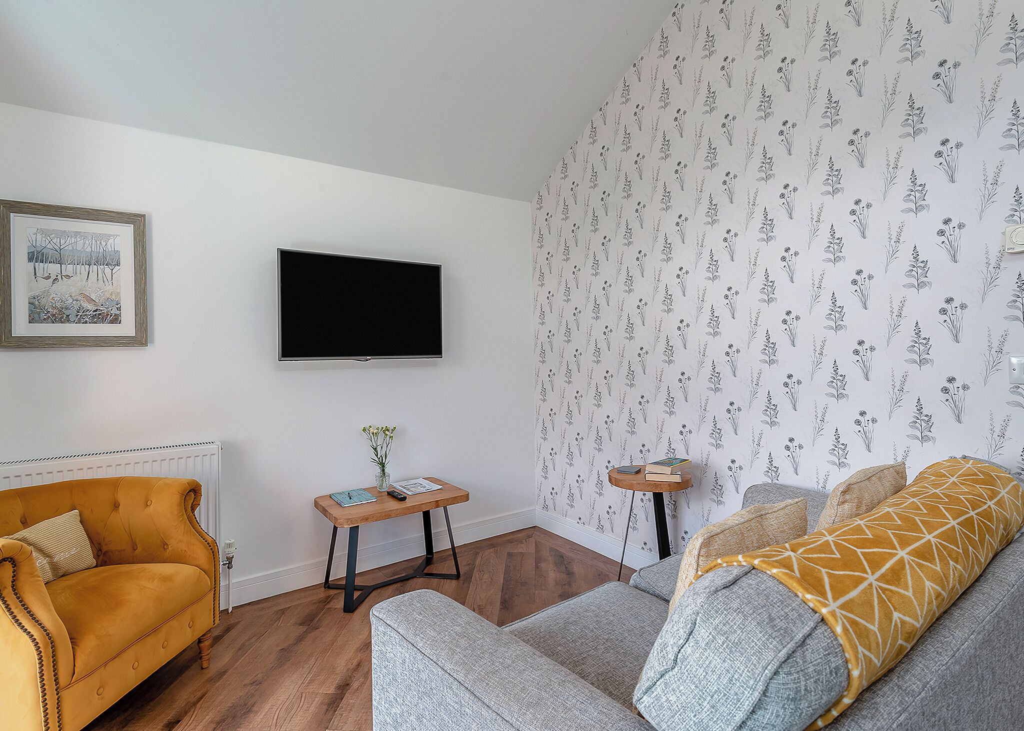 Un salon avec un canapé, une table basse, un téléviseur et un papier peint à motifs.