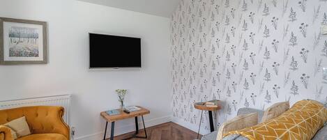 Una sala de estar con sofá, una mesa de centro, televisión y un papel tapiz estampado.
