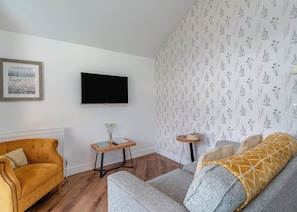 A living room with a sofa, a coffee table, a TV, and a patterned wallpaper. - Stunning lodge with one king-size double and en suite shower. (Orby)